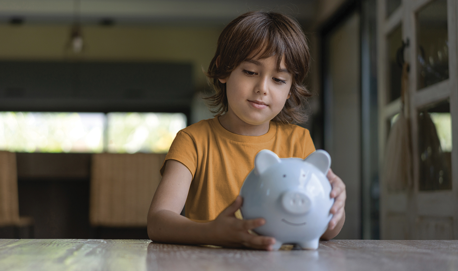 child sitting at a kitchen table , holding a piggy bank